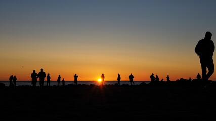 Fototapeta na wymiar Romantic landscape. Silhouettes of people seeing off the sun on the seashore against the backdrop of a colorful sunset.