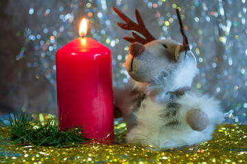 Closeup of the cute soft toy in a form of a deer with tinsel and burning red candle. Winter...