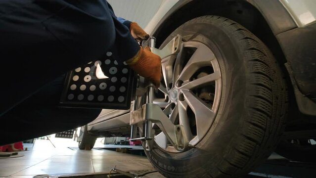 Auto mechanic installing sensor during suspension adjustment and automobile wheel alignment work at repair service station. Close up
