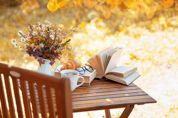 Bouquet of flowers, croissant, cup of tea or coffee, books on table in autumn garden. Rest in garden, reading books, breakfast, vacations in nature concept. Autumn time in garden on backyard