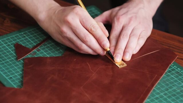 Man tailor cutting artificial leather with ruler close-up. Craftsman carving cowhide at workplace table, making hand made products made of genuine animal leather. Professional atelier.