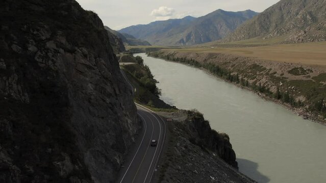 Mountains valley of Altai with traffic cars on Chuya highway and Katun river, Siberia, Russia. Beautiful summer nature landscape at during daytime. Aerial view from a drone