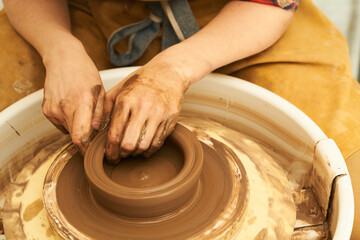 A Potter works with red clay on a Potter's wheel in the workshop..Women's hands create a pot. Girl sculpts in clay pot closeup. Modeling clay close-up. Warm photo atmosphere