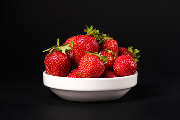 Red fresh strawberries in a white plate on a black background. Summer seasonal berries, close-up