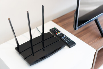 Wife router with three antenna and TV remote control place on the white cabinet - obrazy, fototapety, plakaty