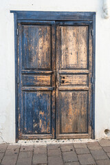 Old chipped solid wood door, natural and blue color, with rusted metal lock, on white wall