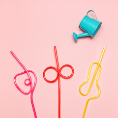 Blue watering can is watering multicoloured straws. Summer concept.