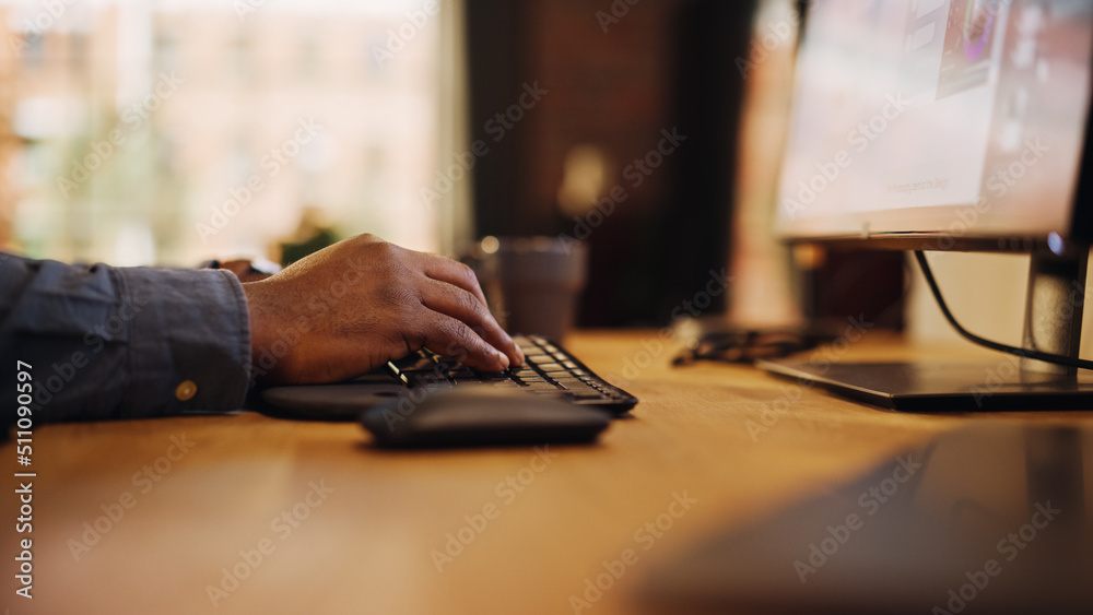 Poster Close Up Footage of Person's Black Hands Use Computer while Sitting at a Table. Creative Designer in a Grey Shirt Using Mouse, Typing on Keyboard. Monitor Display and Laptop on a Desk.