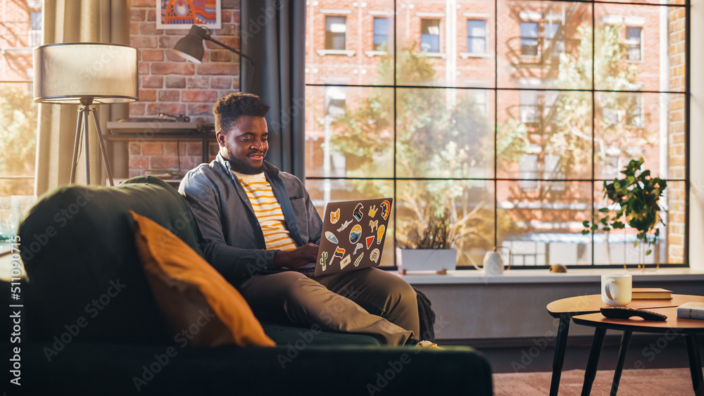 Aufkleber young handsome black man working from home on laptop computer in sunny stylish loft apartment. creat