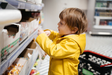 child in the market with a grocery cart, puts sweets in a bag