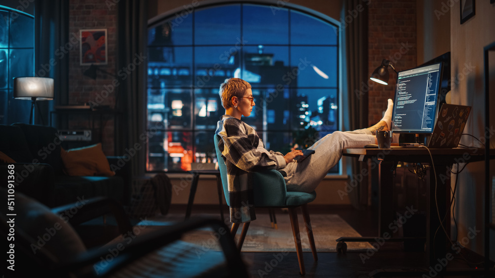 Poster young woman writing code on computer in stylish loft apartment in the evening. creative female weari