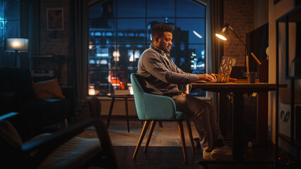 Young Handsome Black Man Working from Home on Laptop Computer in Stylish Loft Apartment in the...