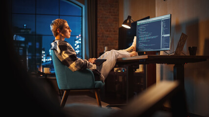Young Woman Writing Code on Computer in Stylish Loft Apartment in the Evening. Creative Female...
