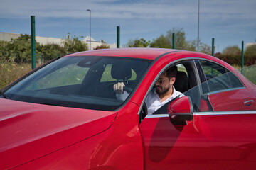 Handsome young man with beard, sunglasses and white shirt, inside his red sports car. Concept beauty, fashion, trend, luxury, motor, sports, winner.