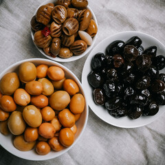 a set of three types of olives in white bowls on a gray napkin - whole large green olives, black olives, green olives grilled in oil, pitted, top view, close-up, fragment