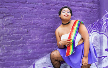 lgbt african american woman with lgbt flag on purple wall background looking at camera smiling