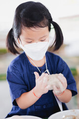 Portrait image child 5 years old. Asian girl learning how to preserve food or make salted egg by plastering white plaster on top of eggshell. Kid wear mask to prevent PM2.5 toxic dust air pollution.