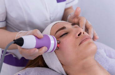 A young woman undergoing a facial radiofrequency face lift treatment. Facial skin care treatment, anti-aging facial rejuvenation. Beauty and dermatology concept.