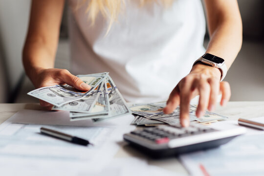 Close up young business woman using counting cash money one hundred dollar bills, checking financial documents, siting at table with papers and tax form, managing planning budget, accounting expenses