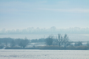 A low-contrast shot of a winter river landscape. A winter landscape of a river or lake from the waterside. A river or lake covered with snow.