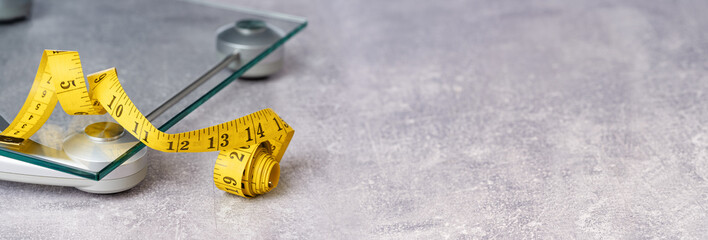 yellow tape measure on top of glass bathroom weighing scale on blue. Front view copy space. Healthy...