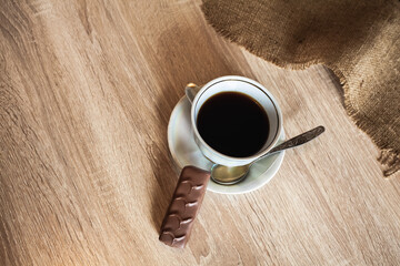 A cup of fragrant black coffee on a saucer with a spoon and a chocolate bar lie on a wooden brown...