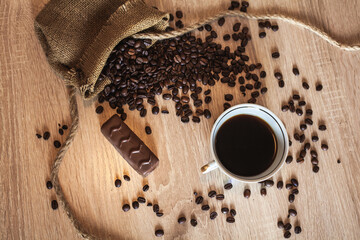 Roasted coffee beans in little bag with ropes and cup of coffee with drink and chocolate on brown...