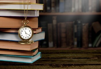 Old clock on a chain with stack books on library background. Retro clock as a symbol of time a...