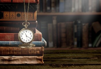 Old clock on a chain with stack books on library background. Retro clock as a symbol of time a...