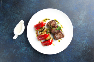 Beef medallions and grilled vegetables. On a gray background.
