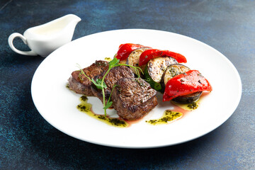 Beef medallions and grilled vegetables. On a gray background.