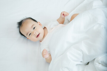 Cute little asian baby lying on bed with soft blanket indoors