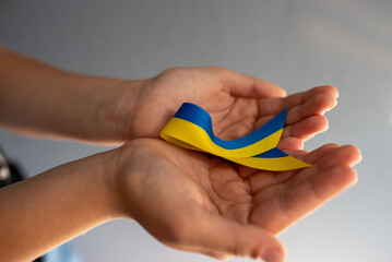 Cropped view of blue and yellow ribbon in young woman's hands on grey background.