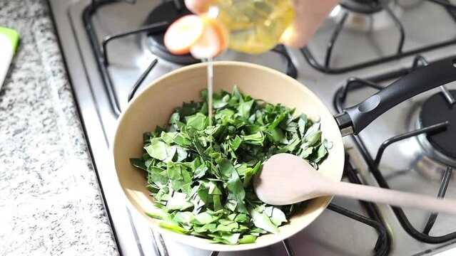 Hands cooking ora-pro-nobis (Pereskia aculeata) and pouring oil into a frying pan, a popular edible plant in Brazil