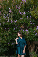 A smiling, sophisticated girl in a turquoise light dress walks in a well-kept green park. It's a hot summer in a tropical country. 