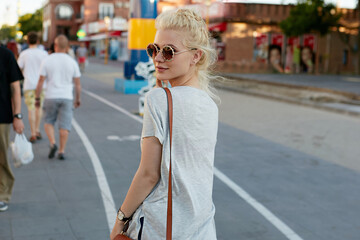 Side view of a young hipster girl with blonde hair, walking alone on the street.