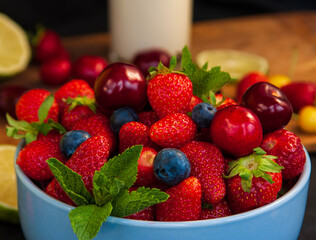 Close-up mix of fresh berries in a bowl - strawberries, cherries, blueberries and mint leaves