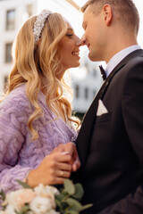 Beautiful young wedding couple in elegant outfits walk around city, smile and kiss on street background. Portrait side view closeup of happy bride and groom in love. Wedding day, family holiday