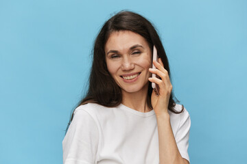 woman talking on the phone pleasantly closing her eyes and smiling broadly while standing on a light blue background with empty space to insert an advertising layout