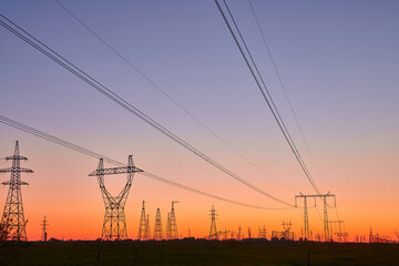 Dark silhouettes of power lines on fiery sunrise. High voltage electricity towers in field and fiery sunset. Concept of crisis of energy consumption, generation, and supply.