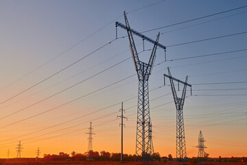 Dark silhouettes of power lines on fiery sunrise. High voltage electricity towers in field and...