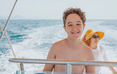 Boy driving a boat with his mother and boat wake in the background. Summer vacation concept 
