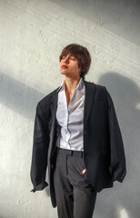 Young thoughtful and sad business woman on background of wall in sun rays, portrait girl in classic suit