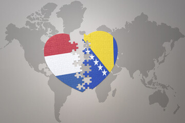 puzzle heart with the national flag of bosnia and herzegovina and netherlands on a world map background.Concept.