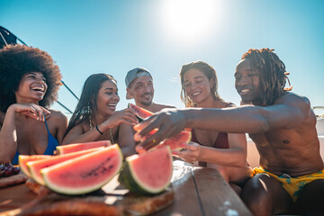 Group of happy friends relaxing and eating water melon while having boat tour in mediterranean sea