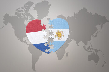 puzzle heart with the national flag of argentina and netherlands on a world map background.Concept.