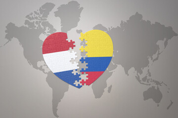 puzzle heart with the national flag of colombia and netherlands on a world map background.Concept.