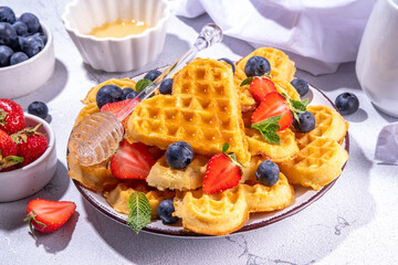 Breakfast belgian waffles with strawberries, blueberries and honey, homemade healthy heart shaped waffles on white kitchen tables copy space