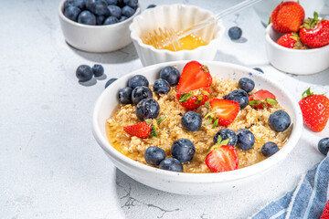 Summer morning oatmeal with berry. Homemade healthy breakfast oats with strawberry, blueberry, honey, nuts and mint on white marble background