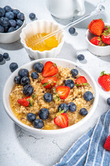 Summer morning oatmeal with berry. Homemade healthy breakfast oats with strawberry, blueberry, honey, nuts and mint on white marble background